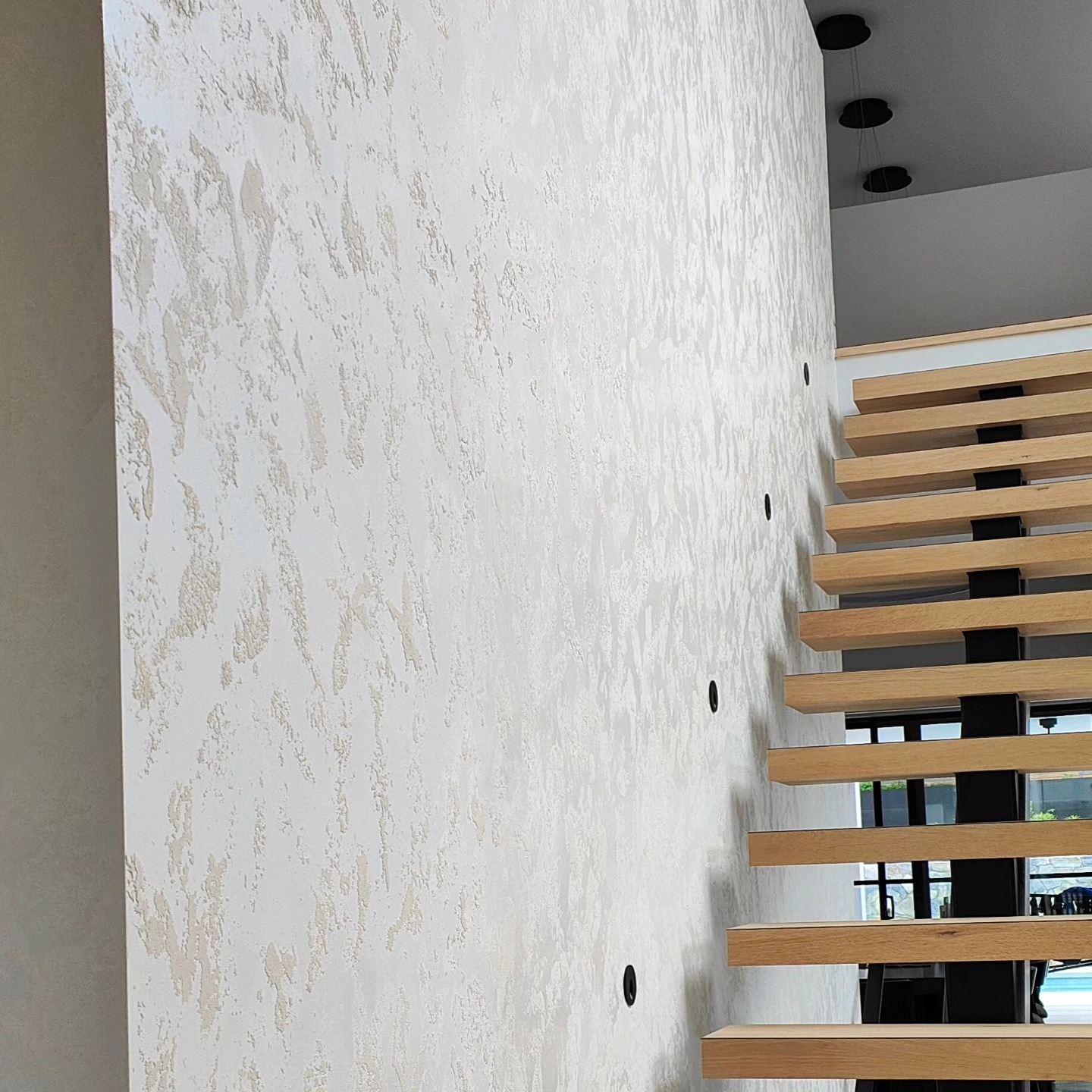 Textured plaster feature wall beside a floating timber staircase in Lugarno