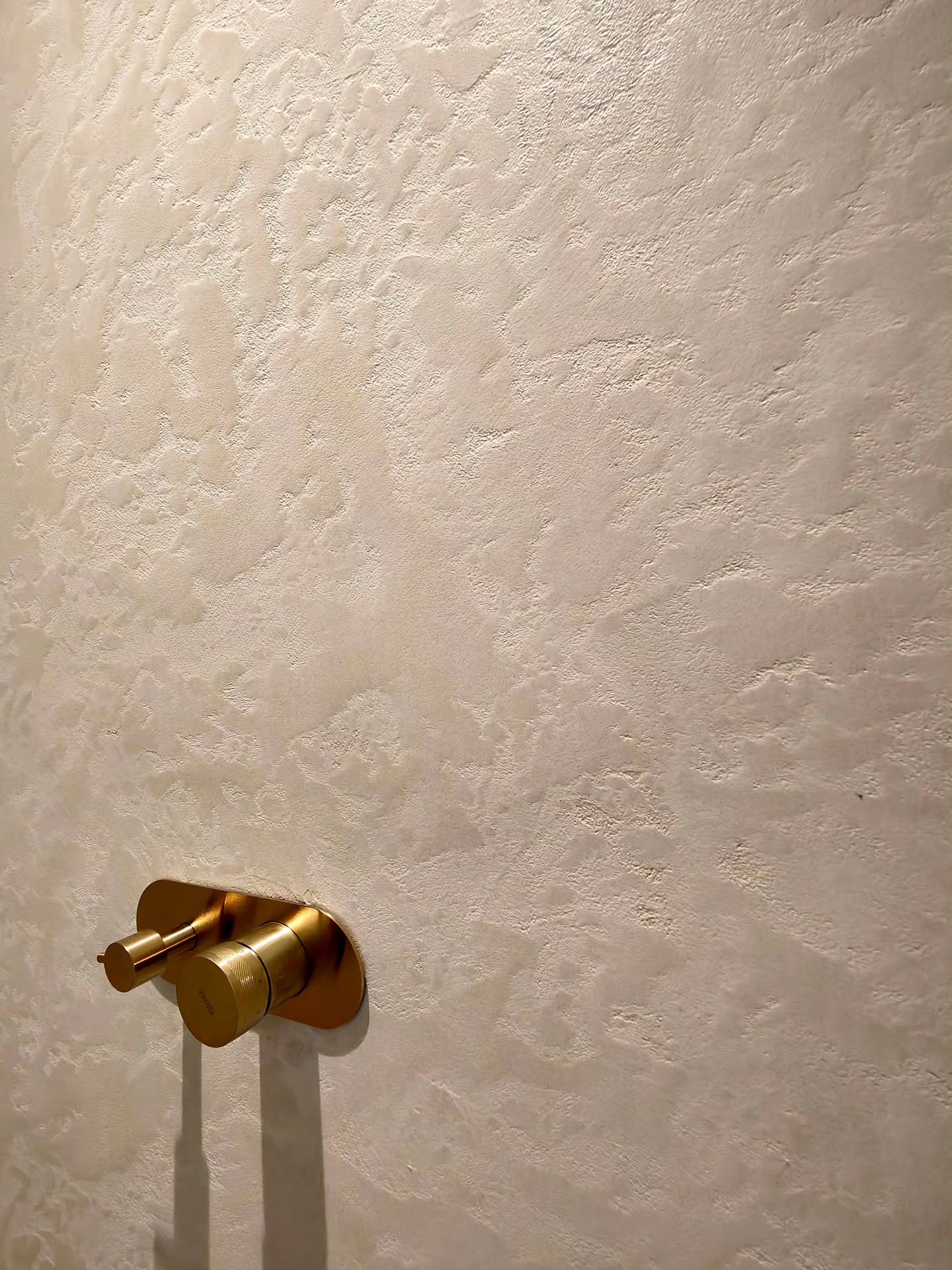 Stamped microcement bathroom wall with a brushed brass mixer